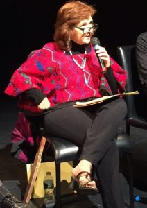 Carmen Tafolla speaks. At her side is the paddle administrators used to hit children in who spoke Spanish in school.